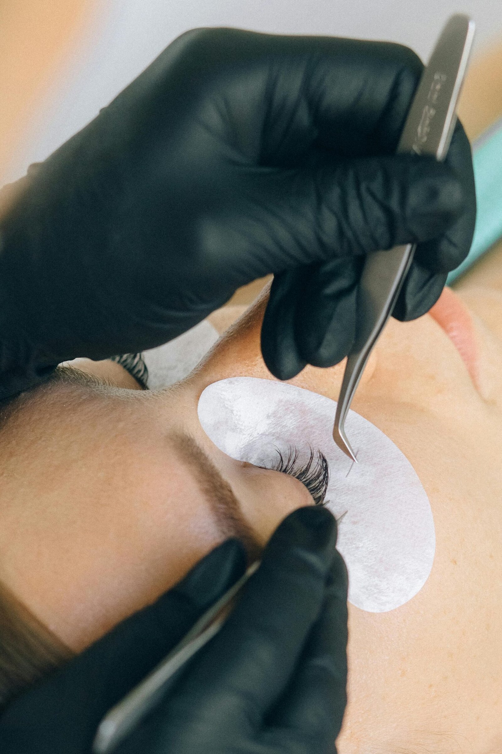 Close-up of eyelash extension application with black gloves and tweezers.